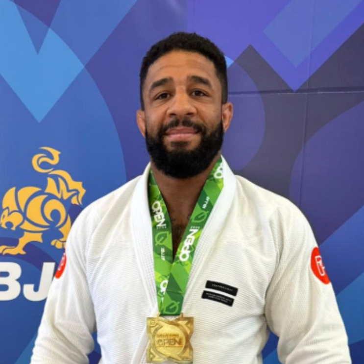 Man in a white judo gi with a gold medal, standing in front of an IBJJF branded background.